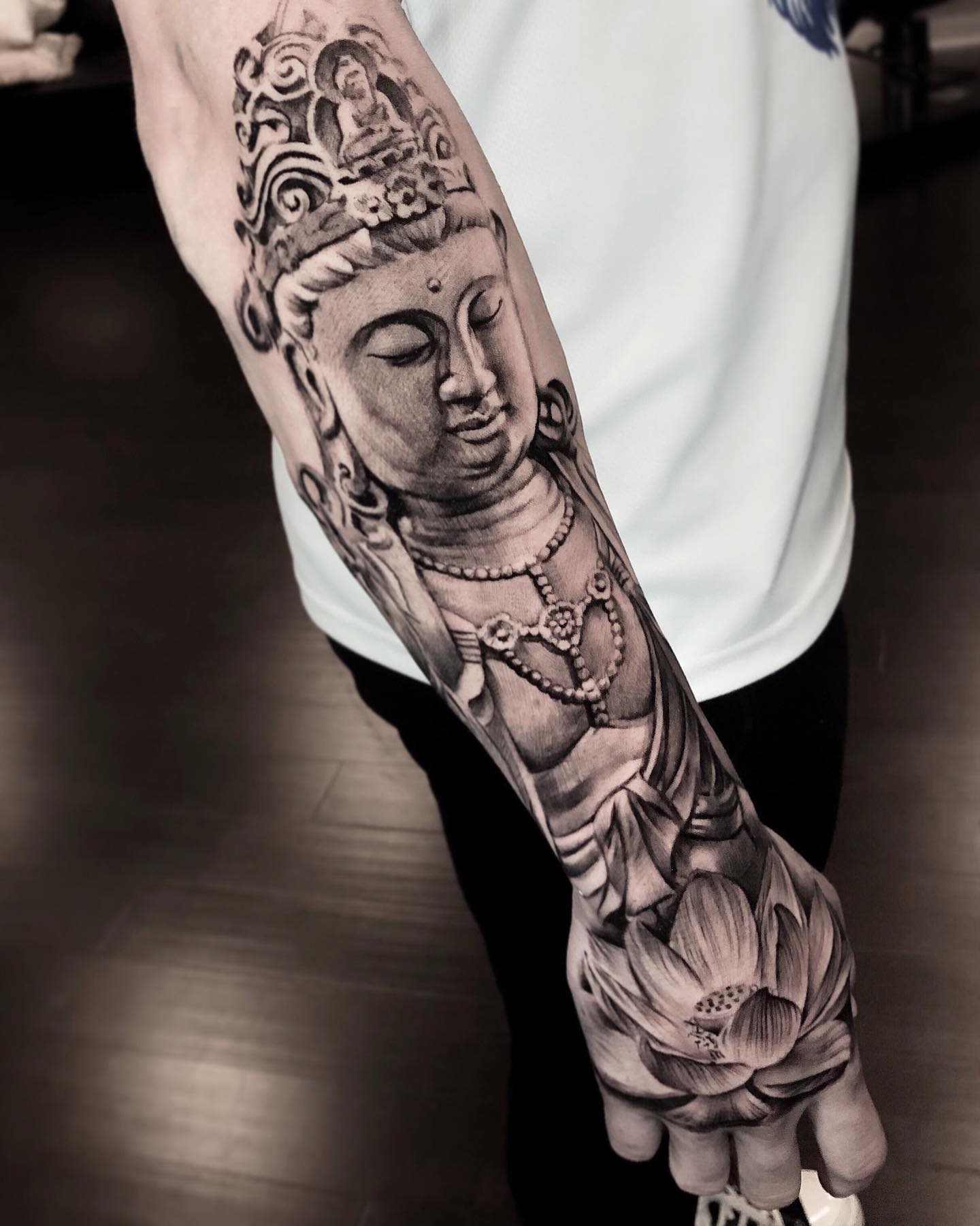 Forearm tattoo of a serene Buddha and detailed lotus on the hand